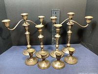 Photo showing the entire set of 8 weighted sterling silver candle holders of varying sizes arranged in a single line against a dark backdrop with a ruler for scale.