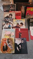 Vinyl record albums spread on floor showing front covers including Johnny Mathis, Ray Charles, Captain & Tennille, Manhattan Transfer, and Marco Jordana.