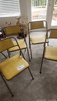 Four yellow vinyl padded folding chairs arranged indoors on carpet, one labeled with seat tag #192