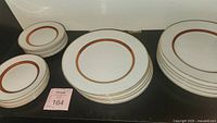 Overview of the stacked dessert and dinner plates showing white porcelain with red and gold border pattern.