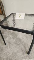 Photo showing angled top view of black framed glass top side table with number card '2' placed on top.