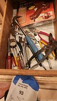 Drawer containing multiple hand tools such as a hammer with a blue handle, wrenches, pliers, and screwdrivers.
