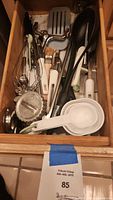 View of kitchen drawer containing varied utensils including spatulas, whisks, measuring cups and cookie cutter.