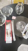 Photo of two clear floral glass bowls, Kool-Aid pitcher, Lenox cake server set in box and glass cake platter on a black table