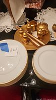Photo of several white plates with gold trim stacked, with gold salt and pepper shakers and gold tapered candles on a gold plate in the background.