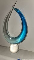 Full view of the Murano glass sculpture showing the elongated loop shape with blue and clear glass sections and white glass base.