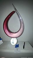 Full view of pink dolphin Murano glass sculpture showing curved body with gradient color from dark pink to light pink and clear pointed tip. Oval clear base supporting sculpture.