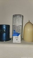 Front view of three pillar candles: blue decorated candle, silver glitter rectangular candle, and cream dome candle