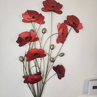 Front view of the tin poppies wall hanging showing vibrant red flowers and golden stems against a white wall.