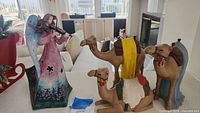 Image showing TinWorks angel figurine playing violin in pink and blue dress standing next to three camel figurines with colorful blankets.