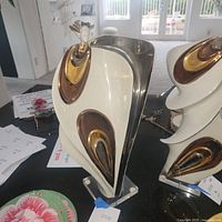 Alternate angle showing both ceramic sculptures together on a table with natural light and background objects.