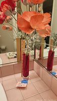 Red glass vase with faux orange poppies and silver-green stems reflected in mirror