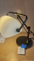 Photo showing white dome-shaped shade, part of black arm and swivel joints of the desk lamp.
