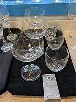 Photo showing various Baccarat stemware and cocktail glasses on black cloth, includes round bowl stemmed glasses and short tumblers.