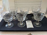 Six stemmed glasses on a black mat with lot tag visible