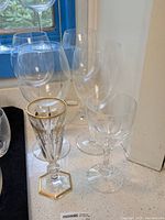 Photo showing a grouping of crystal wine goblets including one gilded goblet with gold detailing and clear goblets behind it.