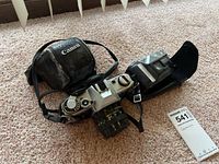 Canon AE-1 film camera with 50mm lens and Canon carrying case, Yashica T3D camera with case, all displayed on carpet.