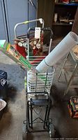 Front view of metal folding cart with wire basket carrying a roll of window film and cardboard box inside the basket, situated in garage.