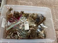 Plastic bin filled with various organza bags containing costume jewelry pieces such as necklaces and bracelets.