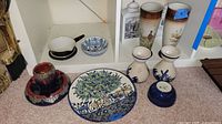 Shelf display of various pottery items including vases, bowls, plates, and a cup and saucer with colorful designs.