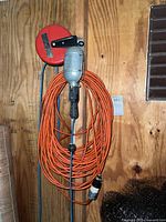 Full image of orange extension cord coiled on red reel with silver work light attached.