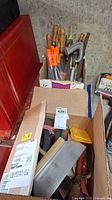 Box with assorted hand files, saw, clamps, and work towels in a garage setting