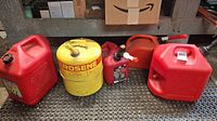 Five fuel cans arranged on a metal shelf: 4 red plastic gasoline cans and 1 yellow metal kerosene can.