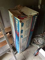 Photo showing the Havahart box with animal trap inside, stored in shed conditions with some storage clutter around it.