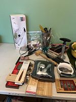 Overall lot displaying various kitchen utensils and tools on a table, including Good Grips mandolin slicer box, glass stein, salt and pepper shakers, and several metal kitchen tools