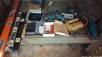 Photo showing 3 spirit levels, drill bit sets in cases, electric drill, and electric cut off tool arranged on floor.