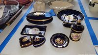 Photo showing multiple Limoges porcelain items on table including trinket boxes, dish, plate, and covered jars in cobalt blue with gilded floral patterns.