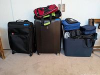 Photo showing multiple luggage items including two large suitcases, a red duffel bag, soft-sided totes, and a large blue plastic storage bin filled with various bags and travel items.