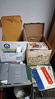 Overview of magazines and brochures in boxes and envelopes, including Chrysler brochures and large envelopes.