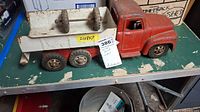 Full view of vintage Buddy-L metal toy truck with white trailer, placed on green surface with visible rust and wear
