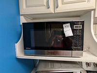 Front view of the Panasonic microwave showing stainless steel and black glass door with control panel and auction tag.