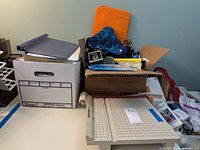 Photo of boxes and office supplies including folders, scissors, and paper cutter on table