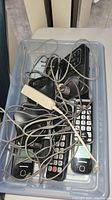 Plastic bin containing tangled phone cords, adapters, and a base unit.