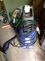 Blue Clean 383 pressure washer with attached power cord and hose, spray gun visible on ground in shed environment.