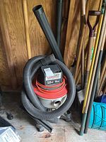 Full view of Rigid Wet Dry Vac with hose and extension tube inside a shed.