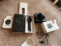 Two smart watches with boxes and accessories on carpeted floor.
