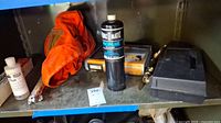 Shelf display of soldering equipment showing orange welding hood, propane fuel bottle, black toolbox, solder wire, and other tools.