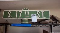 Front view of the weathered S. 17TH ST. pole top street sign with visible raised white letters on green background.