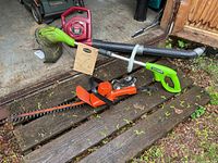Photo shows the three tools: Greenworks weed whacker with manual, Black & Decker hedge trimmer, Toro blower, laid out on wooden steps near shed.