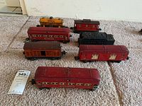 Seven vintage train cars arranged on carpet floor including passenger cars, boxcars, tanker, and coal tender.