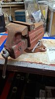 Photo of the full bench vise showing rust, red paint, handle bent downward.