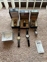 Six wristwatches arranged on carpet, three in original boxes and three loose on lower row
