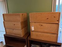 Six wooden wine boxes stacked in two groups of three on wooden furniture with window background.