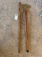 Two wooden canes laid side by side on carpeted floor, one with carved head, one with metal dog-shaped head.