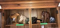 Shelf with nine animal figures including wooden, ceramic, and metal pieces such as moose, horses, elephant, rhino, and dolphin.