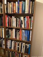 Photo of shelving unit with multiple shelves containing a large collection of varied books in different sizes and colors, including fiction, literature, and history genres.